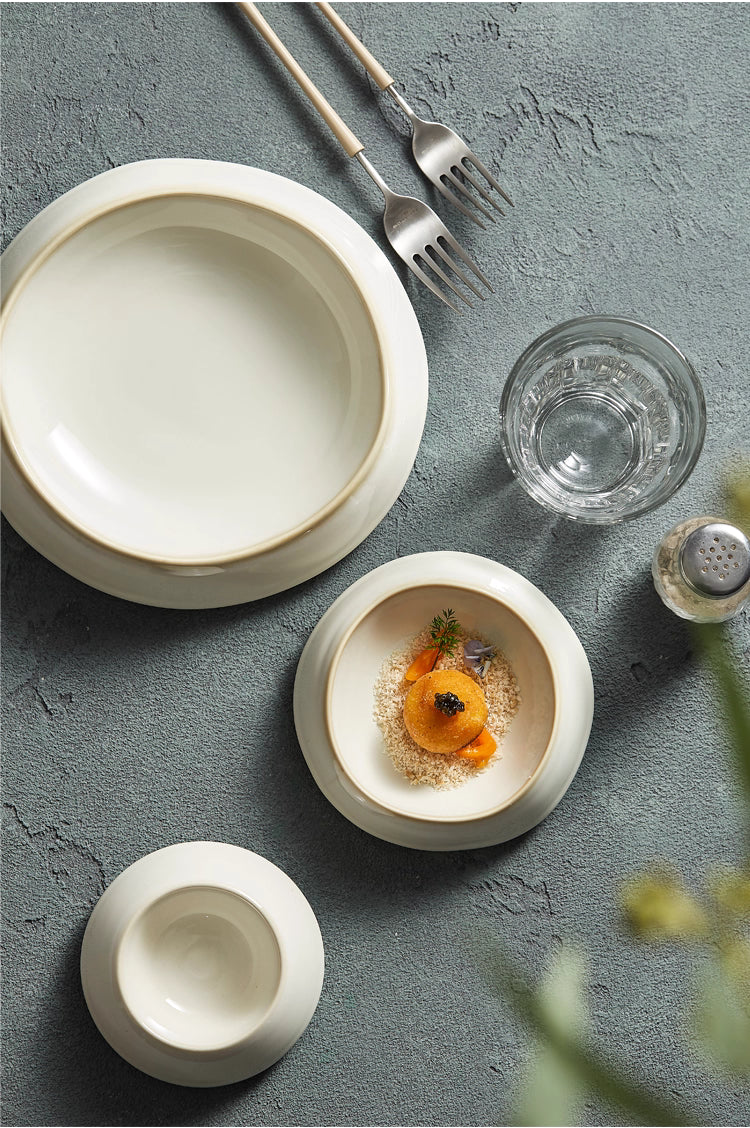 Dining setup with white ceramic plates, a glass, and silverware on a gray surface.