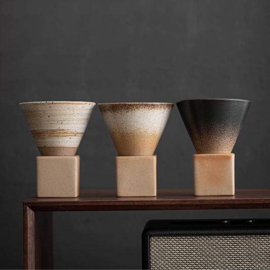 Three coffee cups of different colors on a wooden shelf against a dark background